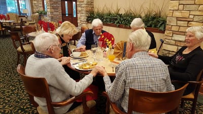 Residents sharing a meal and holding hands in a dining room