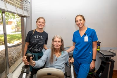 Two staff members smiling with a resident in a rehabilitation activity
