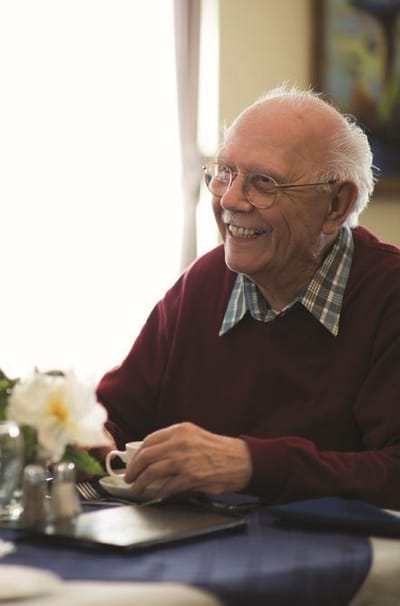 A smiling elderly man enjoying a cup of coffee