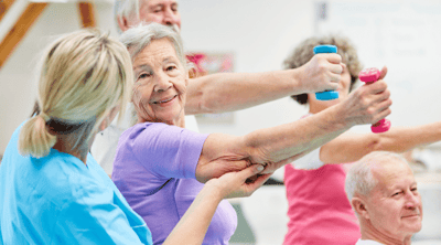 Elderly residents engaging in exercise activity with staff assistance.