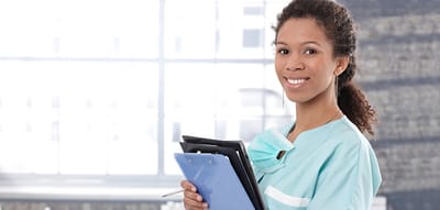 A nurse smiling while holding a clipboard