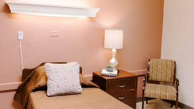 A well-furnished private resident room with a bed and chair