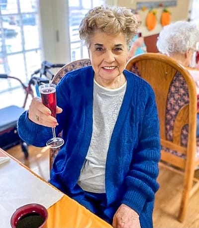 A resident smiling and toasting with a drink in a communal area