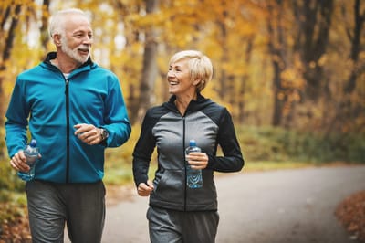 Couple jogging in a forested area with autumn leaves