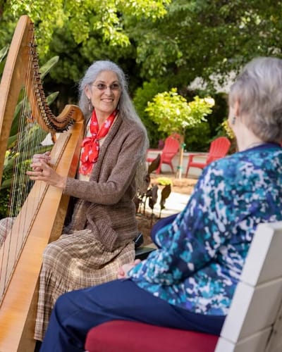 Resident playing harp for another resident outdoors