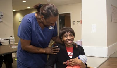 Magnolia Manor of Marion County, Nursing Home in Buena Vista, GA — Caregiver assisting a smiling senior resident in a communal area