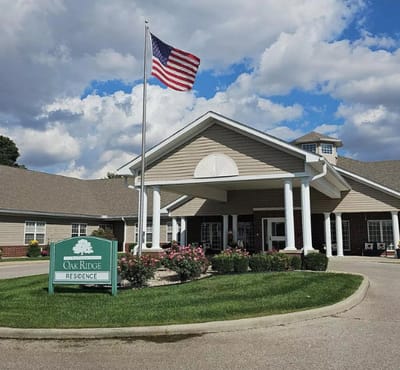 The Villages at Oak Ridge, Nursing Home in Washington, IN — Oak Ridge senior living facility entrance with flag and flowers