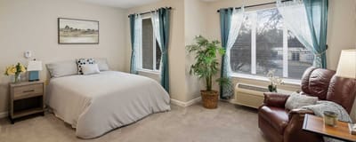 Well-decorated private resident room with a bed and chair