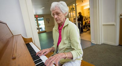 A resident playing piano in a bright activity room