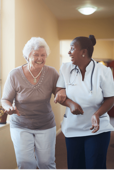 A smiling senior resident and nurse walking together