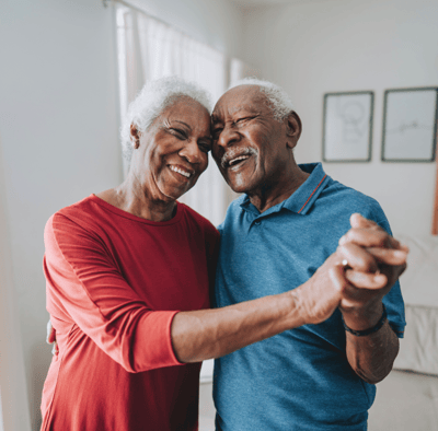 A happy elderly couple dancing together indoors