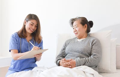 Nurse taking notes by a smiling resident in bed