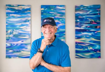 Smiling resident wearing a St. Mark cap in front of artwork