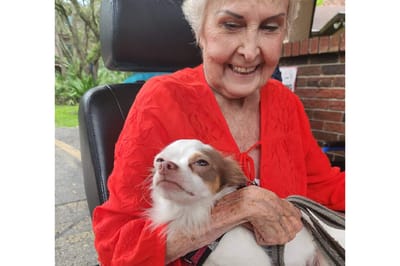 Resident smiling with a small dog in an outdoor setting