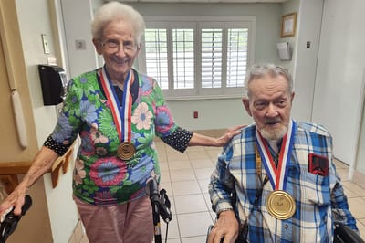 Two residents wearing medals in a facility hallway