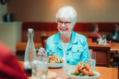 A smiling elderly woman enjoying a meal in the dining room.