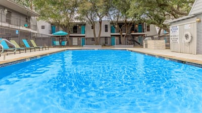 Swimming pool surrounded by trees and lounge chairs