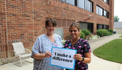 Two staff members holding a sign outdoors