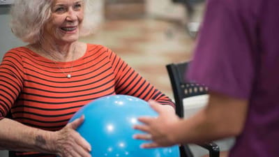 A senior woman smiling while holding a blue exercise ball