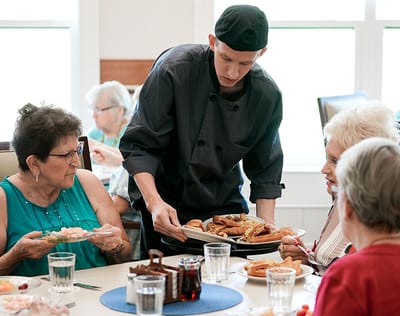 Residents enjoying a meal served by staff in a dining room