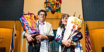 Two individuals holding Torah scrolls in a facility interior