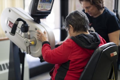 Resident exercising with staff assistance in a fitness area