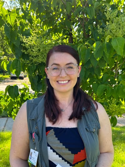 Staff member smiling outdoors near greenery