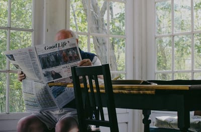 An elderly man reading a newspaper in a sunlit room