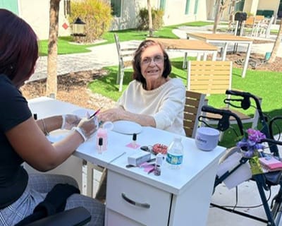 Resident enjoying a manicure outdoors with staff assistance.