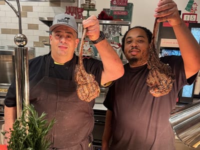 Two chefs holding grilled meat in a kitchen