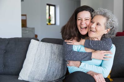 Two women laughing and embracing on a couch