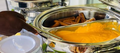 A hand serving food from a buffet tray.