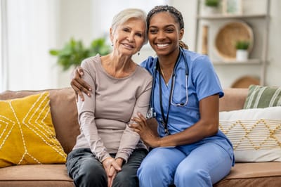 A caregiver and resident smiling together on a sofa
