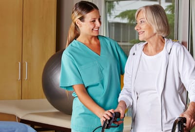 Carrollton Nursing & Rehab Ctr, Nursing Home in Carrollton, GA — Caregiver assisting elderly woman with walker indoors