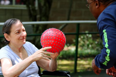 Resident playing with a red ball outdoors with staff member
