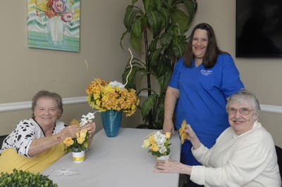Carrollton Nursing & Rehab Ctr, Nursing Home in Carrollton, GA — Women arranging flowers with a caregiver in a cheerful room