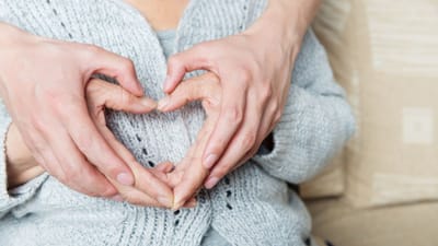 Two hands forming a heart shape over elderly hands