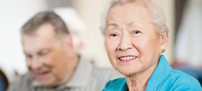 A senior woman smiling with a man in the background