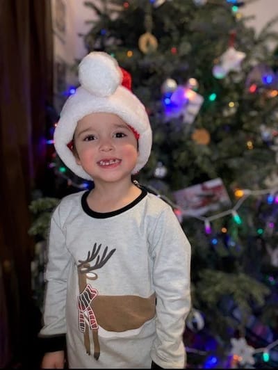 A smiling child in a Santa hat by a Christmas tree