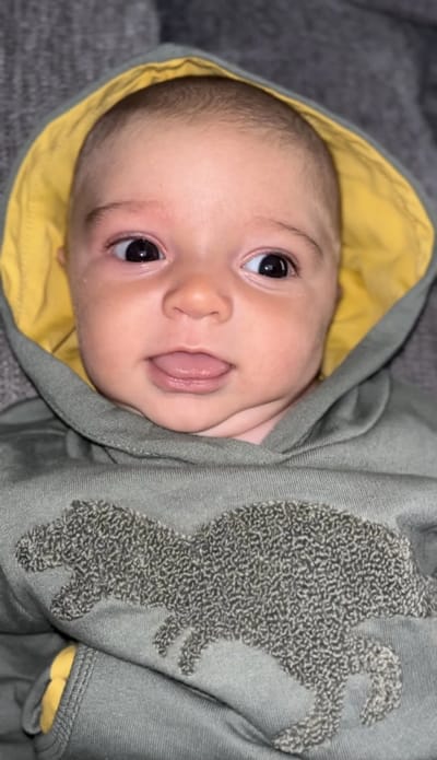 A smiling baby in a hoodie with a dinosaur design