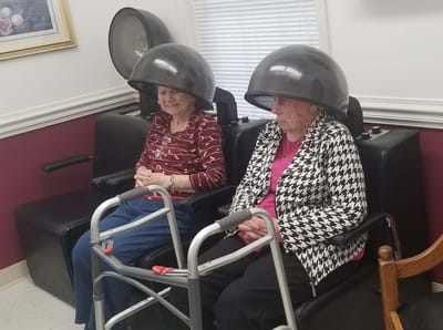 Two residents in hair dryers in a salon area
