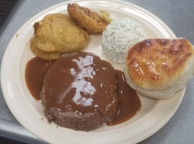 A plated meal featuring meatloaf, sides, and a biscuit