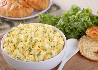 A bowl of egg salad with croissants and lettuce