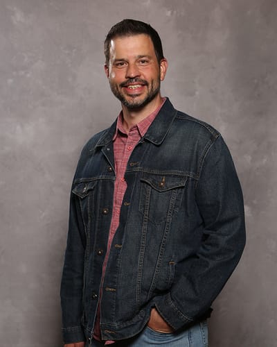 The Gardens at Calvary Alc, assisted living in Columbus, GA — Man smiling in a denim jacket against a gray backdrop