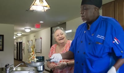 Chef preparing a meal with a resident in a dining area