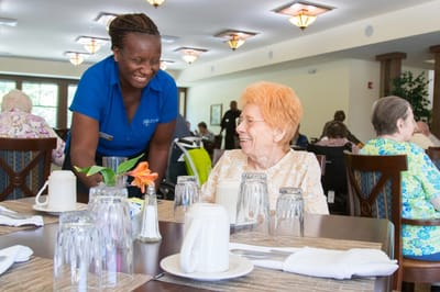 A smiling staff member serving a resident in the dining room