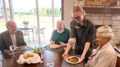 Residents dining together with staff serving meals