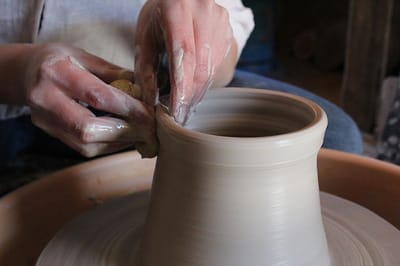 Person shaping a clay pot on a pottery wheel