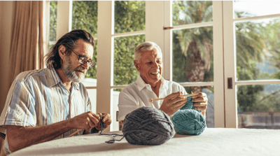 Two senior men crocheting together in a bright room