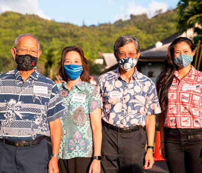 Four individuals wearing masks and vibrant shirts posing outdoors